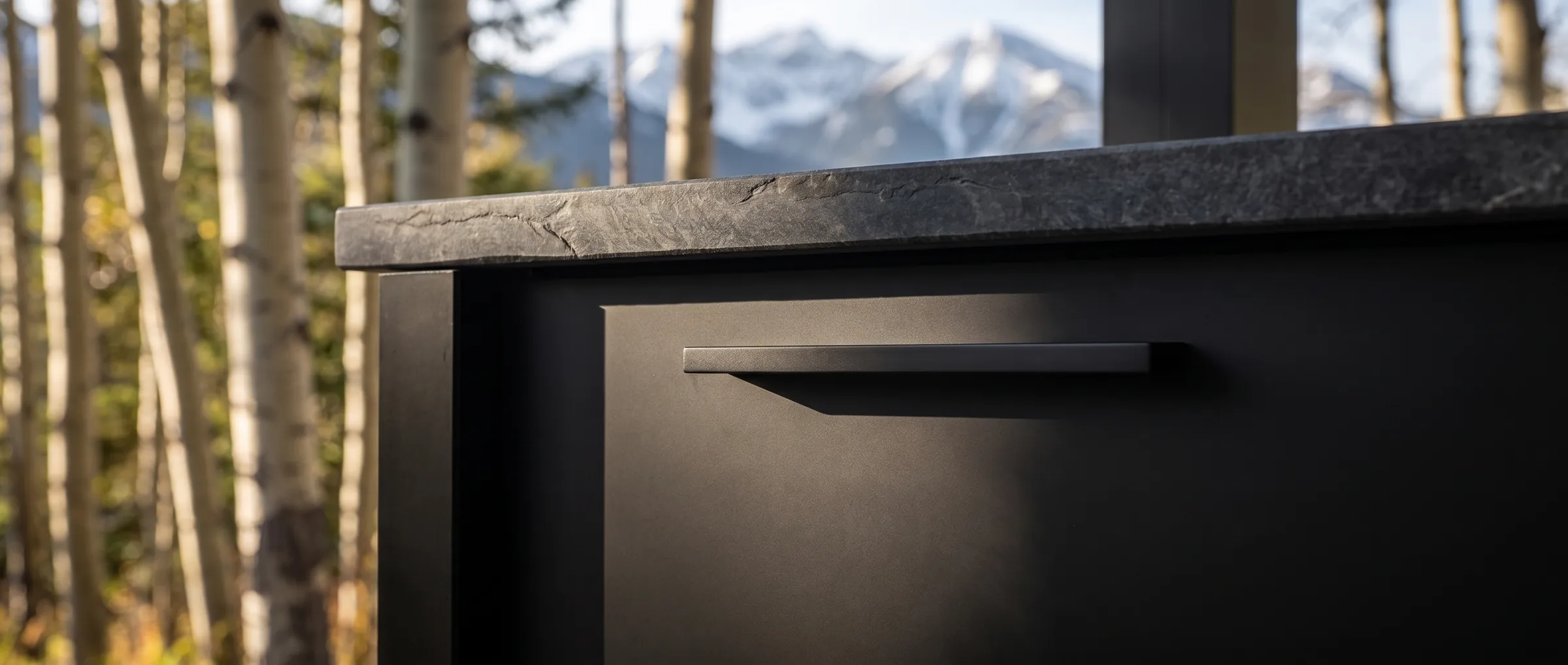 Close detail of a matte black cabinet front, recessed bar pull and dark stone counter edge